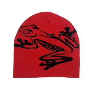 Detailed close-up of a red knit beanie featuring a large black abstract frog jacquard pattern