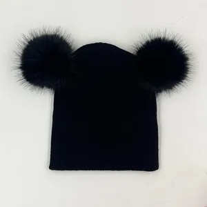 Détail d'un bonnet en maille noire avec deux grands pompons en fausse fourrure douce