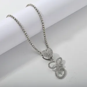 Close-up of silver tennis chain necklace with iced-out heart and cursive letter pendant