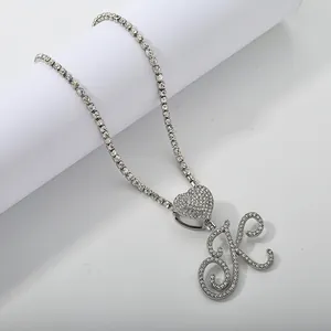 Detail of silver tennis chain with iced out heart and cursive letter K pendant