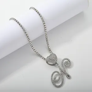 Detail of silver tennis chain with heart accent and iced-out cursive letter H pendant