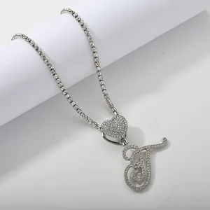 Detail of silver tennis chain featuring a iced-out heart and cursive letter T pendant