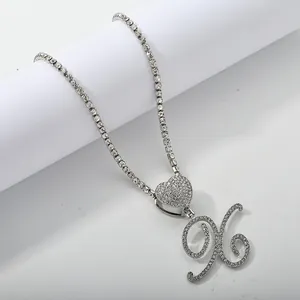 Macro detail of silver tennis chain with iced out heart and cursive letter X pendant