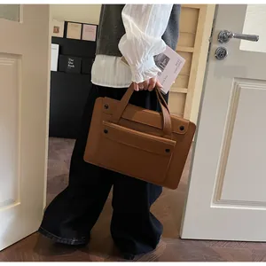 Brown leather tote bag featuring long handles and front pocket for commute and work