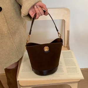 Retro brown suede bucket bag with gold emblem and top handle on a wooden surface