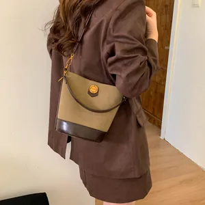 Retro khaki suede bucket bag with brown leather trim and golden hardware worn by a model