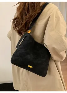 Close-up of black frosted leather hobo bag with gold hardware worn over a beige trench coat