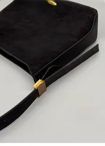 Close-up of golden metal adjustment buckle and holes on black matte leather shoulder strap