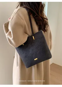 Detail der grauen Wildleder-Tote Bag mit weißer Naht und goldener Schließe am Modell