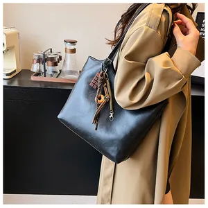 Dettaglio di una grande borsa tote in ecopelle nera con nappa e charm in un caffè