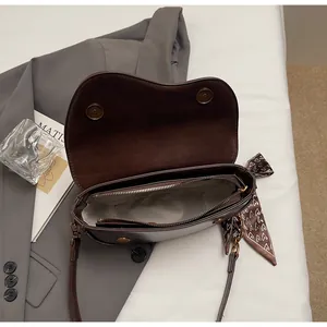 Detail of dark brown leather saddle bag with silk scarf and magnetic closures