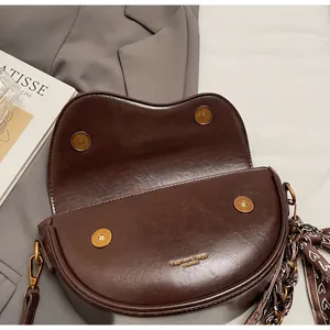 Detail view of dark brown saddle bag showing gold magnetic snaps and floral scarf accessory