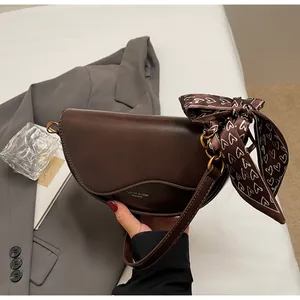 Detail of dark brown saddle bag with golden logo, contrast stitching and heart silk scarf