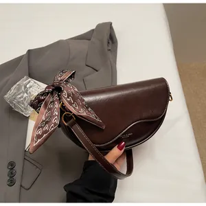Detail of a dark brown saddle bag with a decorative scarf and fine stitching on the flap