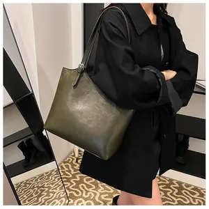 Dettaglio di una grande borsa tote verde oliva in pelle indossata con un cappotto nero