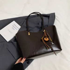Dettaglio della borsa tote in pelle marrone scuro con ciondolo etnico su giacca blu