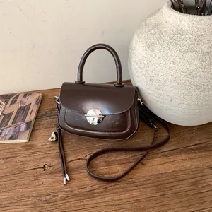 Detailed close-up of dark brown vintage saddle bag with silver metal lock on wood surface