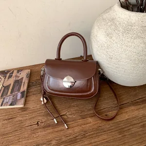 Detail of a brown vintage saddle bag with silver buckle and tassel on a wooden desk