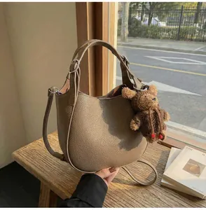 Detail of khaki brown lychee leather handbag with a cute teddy bear charm and strap
