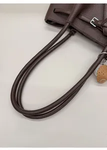 Detalle de bolso tote de cuero granulado café con asa ancha y colgante de guante de béisbol