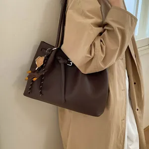 Detalle de bolso tote de cuero marrón con borlas largas y un colgante de osito