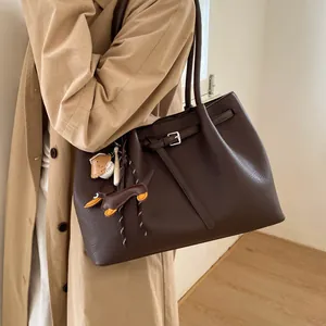 Detalle de bolso tote en cuero granulado marrón oscuro con hebilla y colgante de perro