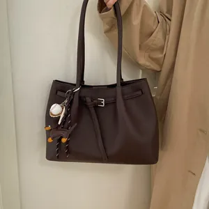 Detalle de bolso tote de cuero granulado marrón oscuro con colgantes de perro y béisbol