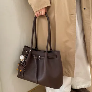 Detalle de bolso tote de cuero marrón granulado con colgante de béisbol y hebilla metálica fina