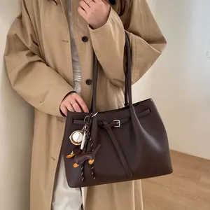 Detalle de bolso tote de cuero marrón con colgantes sobre una gabardina larga clásica