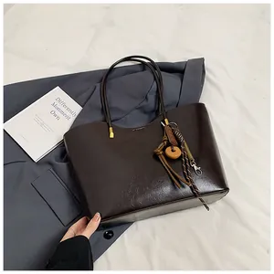 Dettaglio di borsa tote marrone scuro lucido con ciondolo decorativo in perline
