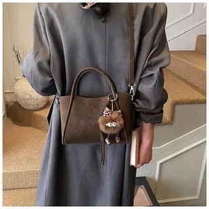 Detail of dark brown suede bucket bag with plush charm on a grey trench coat model