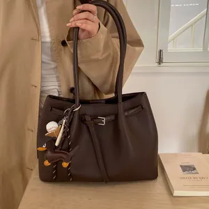 Detalle de bolso tote marrón oscuro con textura de grano y colgante de perro salchicha