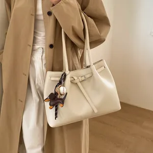 Detalle del bolso tote de cuero crema con dijes elegantes combinado con una gabardina