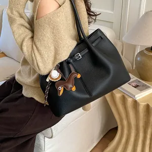 Detalle del bolso tote de cuero negro con colgantes de béisbol y un perro salchicha