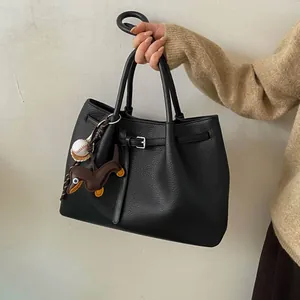 Detalle de bolso tote de cuero negro con colgante de perro salchicha y hebilla metálica