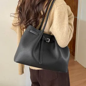 Detalle del bolso tote negro con textura de guijarros y hebilla en una modelo