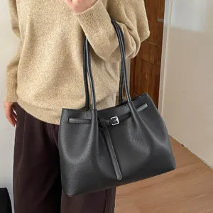 Detalle de bolso tote negro en cuero granulado con hebilla plateada llevado por una modelo