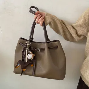 Detalle de bolso tote en cuero granulado marrón oliva con colgante de perro salchicha