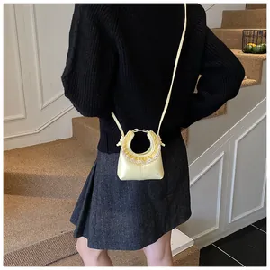 Detail of light yellow mini crossbody bag featuring ruffled lace trim and embossed logo