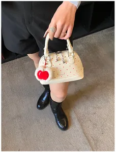 Detail der weißen gepunkteten Muscheltasche mit Silberreißverschluss und rotem Apfel-Anhänger