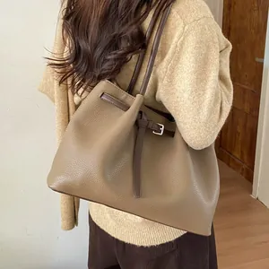 Detalle del bolso tote taupe con textura litchi y hebilla en el hombro de la modelo