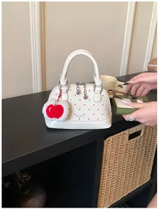 Detailansicht einer weißen Muschel-Minihandtasche mit roten Punkten und Apfelanhänger