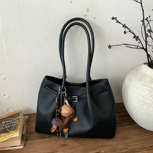 Detalle de bolso tote negro de cuero granulado con un colgante de perro salchicha marrón
