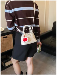White shell bag with red polka dots and heart charm shown being worn by a model