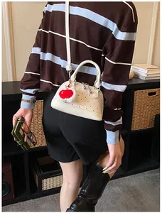 Mini-Schalentasche in Beige mit roten Punkten und Kirsch-Anhänger am Modell getragen