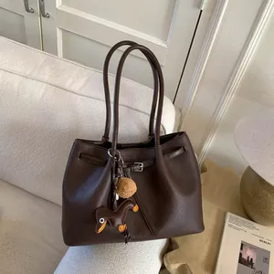 Detalle de bolso tote de cuero marrón oscuro con hebilla plateada y colgante de perro fiel