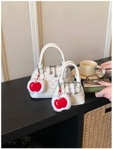 Detailansicht der weißen Boston-Tasche mit roten Punkten und rotem Plüsch-Apfel-Anhänger