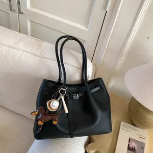 Detalle de bolso tote de cuero negro con colgantes de teckel y béisbol sobre un sofá