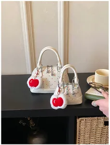 Detail view of two white shell handbags with red polka dots and apple charms on a desk