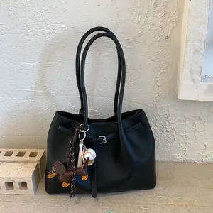 Detalle de bolso tote negro de cuero granulado con colgante de perro salchicha y béisbol